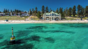 A coastal building with a green roof and arched windows, situated near a beach with clear turquoise water. - Ocean Views Apartment – Relax, Recharge & Enjoy the View (Cottesloe)