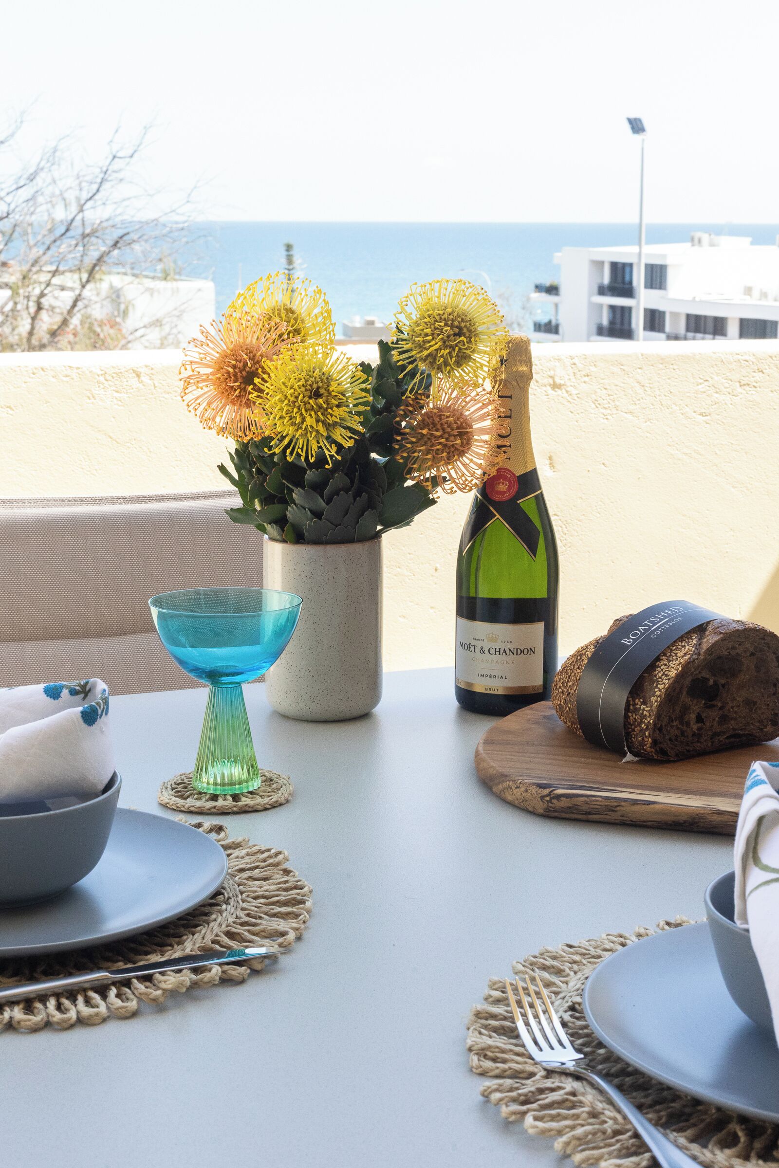 A table set with a bottle of champagne, a loaf of bread, a bowl, and a glass.
