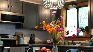 Una cocina moderna con armarios oscuros, un microondas de acero inoxidable, una mesa de comedor de madera con un cuenco de fruta y un jarrón decorativo con flores.