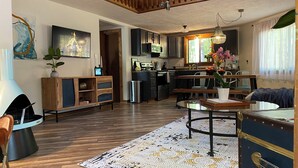 Una cocina moderna con armarios de madera, una zona de comedor con una mesa redonda y una sala de estar con sofá y chimenea.