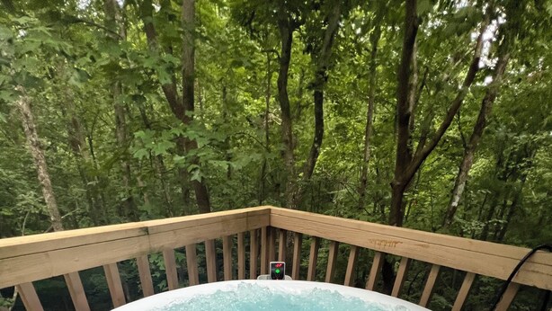 Un jacuzzi rodeado por una terraza de madera con un bosque de fondo.