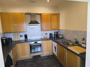 A compact kitchen with wooden cabinets, a built-in oven, a washing machine, and a coffee maker.