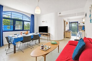 A living room with a red sofa, a dining table with chairs, a TV, and a large window with blue curtains. - Villetta Pino Pool & Sea w/Terrace, Nardò, Italy (Nardò)