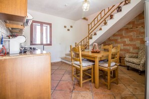 A kitchen with a wooden table and chairs, a staircase with a brick wall, and a window with blinds.
