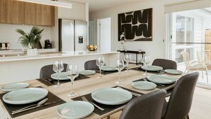 Una cocina moderna con armarios blancos, horno empotrado y comedor para seis personas, con una mesa larga, sillas y copas de vino.