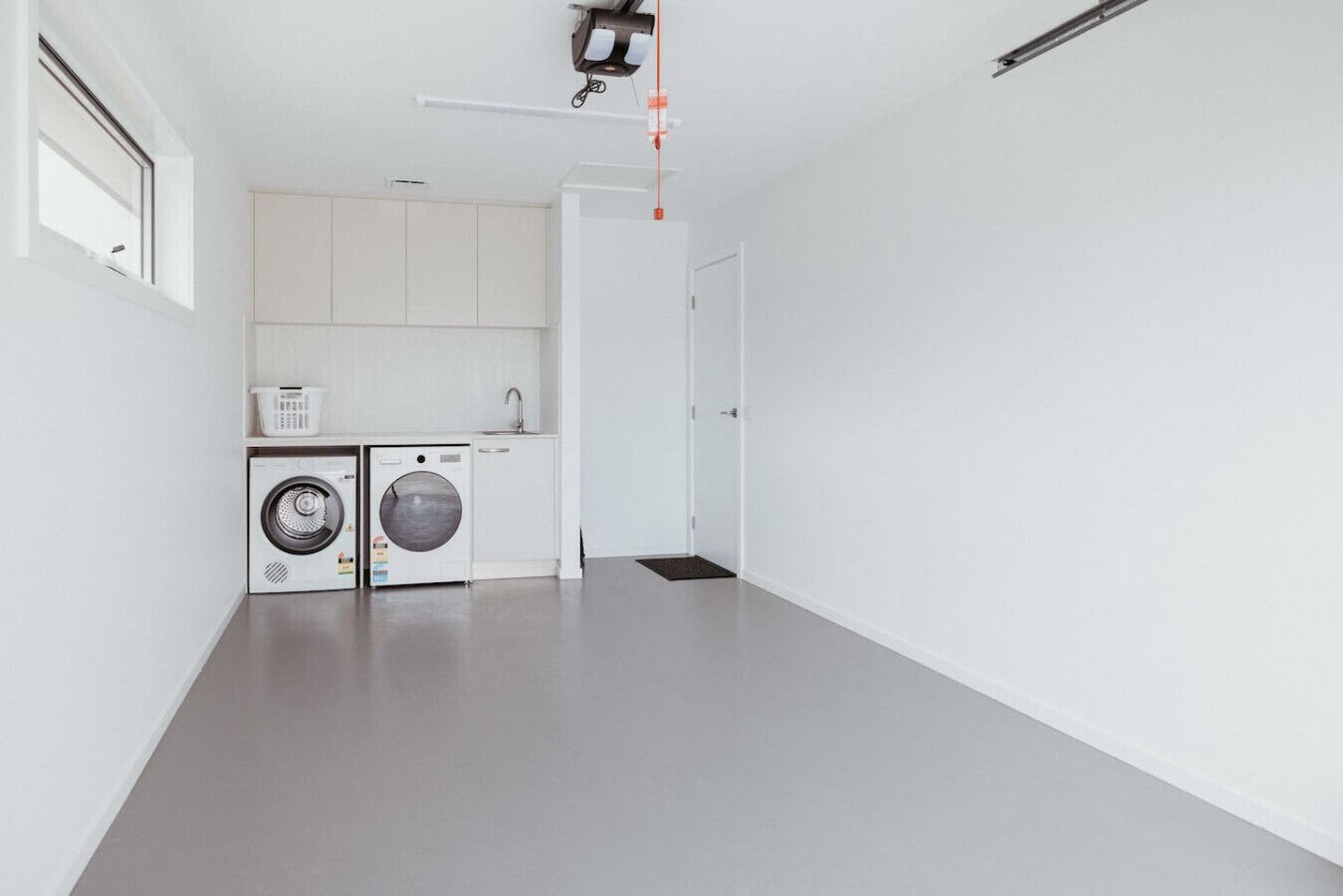 A laundry room with two washing machines, a drying rack, and a small sink.