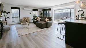 Ein modernes Wohnzimmer mit grauem Sofa, einem runden Couchtisch und einer Küchenzeile mit Barbereich.