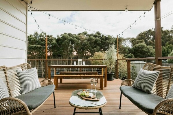 An outdoor deck with wicker furniture, a glass table, and a wooden bench.
