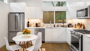 Une cuisine moderne avec des meubles blancs, des appareils en acier inoxydable et un coin repas comprenant des chaises et une table, le tout dans des tons blancs.