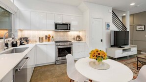 Une cuisine moderne avec des armoires blanches, un four à micro-ondes encastré et une cuisinière. On y trouve un coin repas avec une table et des chaises blanches, ainsi qu'un vase rempli de tournesols.