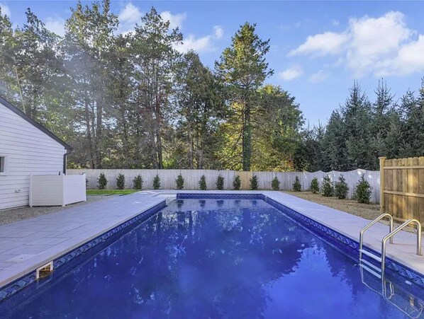 Une piscine rectangulaire à l’eau d’un bleu limpide, entourée d’une terrasse en bois et d’un petit muret en pierre.