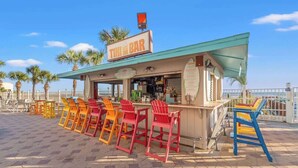 Un bar tiki con asientos al aire libre y vista despejada a la playa.