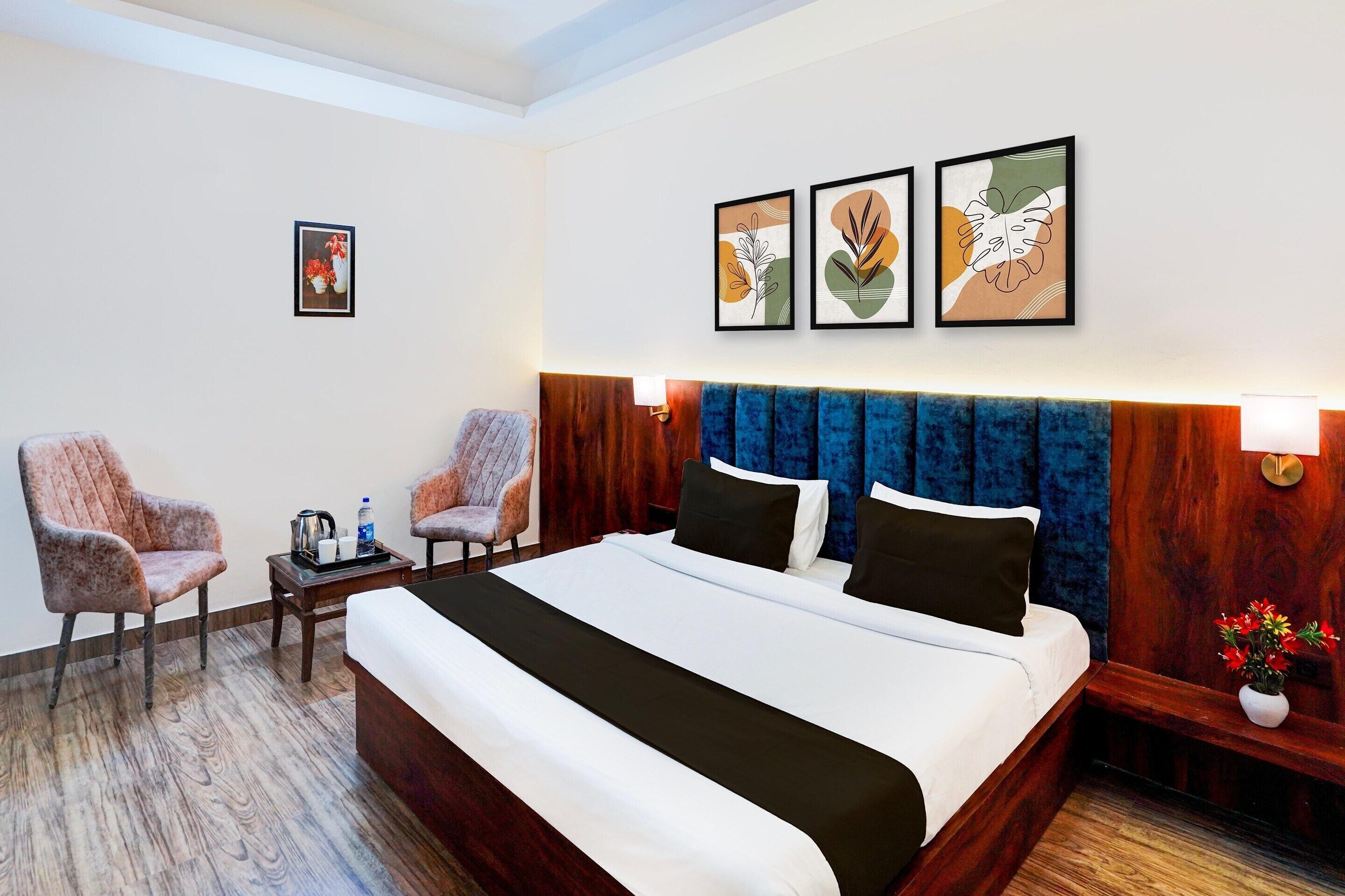 Ein Hotelzimmer mit einem großen Bett, zwei Sesseln, einem kleinen Tisch mit Wasserkocher und einem Nachttisch mit Lampe.