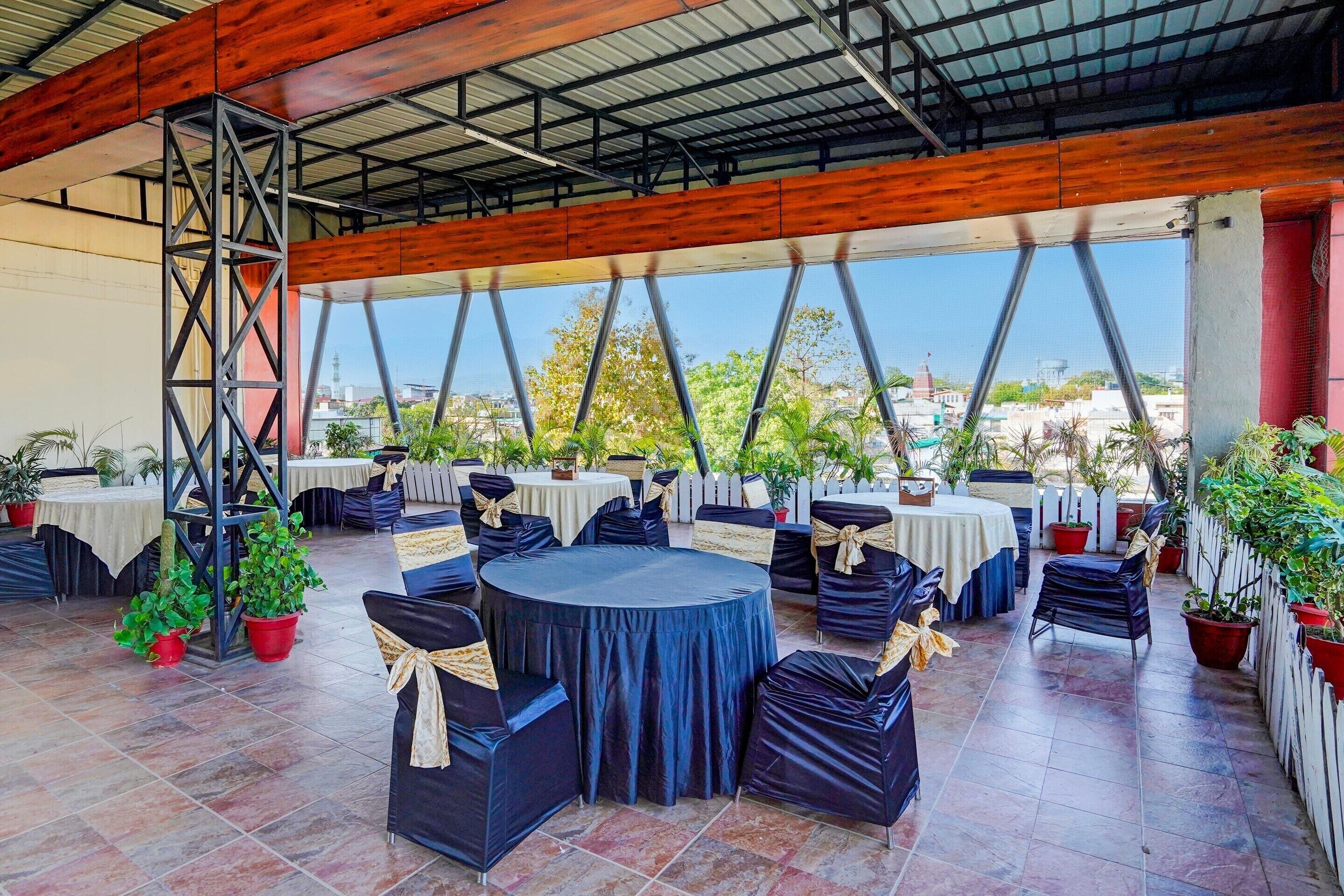An outdoor patio area with round tables and chairs, potted plants, and a view of the cityscape.