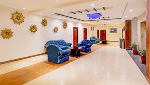 A hotel lobby with a reception desk, blue sofas, and decorative wall art. - Classic Hotel Kolam (Dehradun)