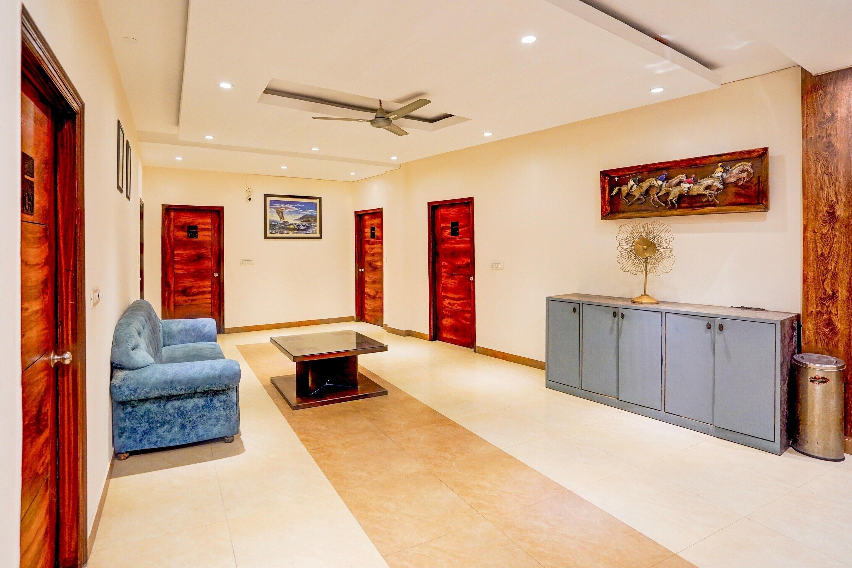A spacious lobby with a blue armchair, a glass-top table, a ceiling fan, and a cabinet with a decorative item.
