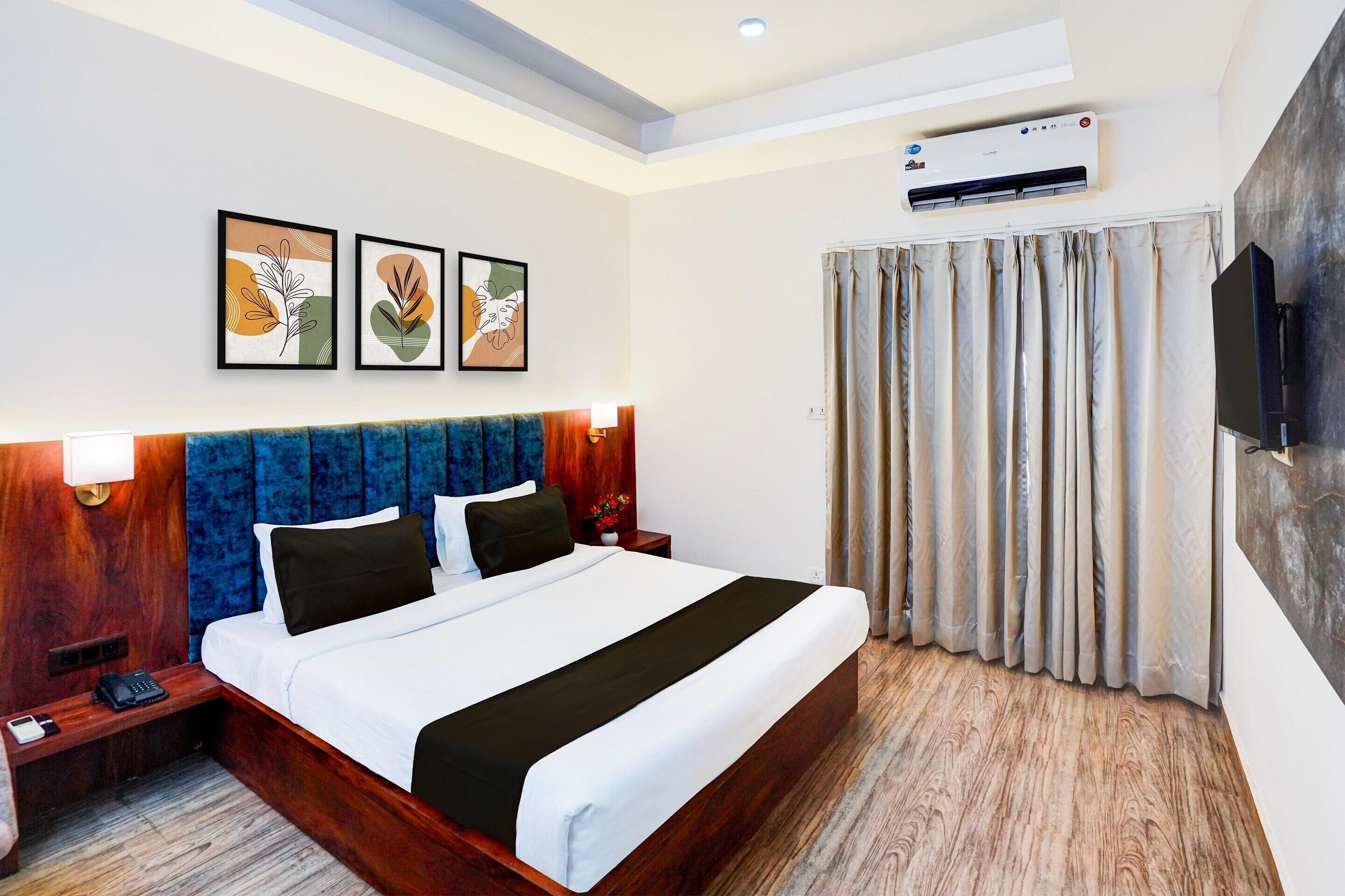 Habitación de hotel con una cama grande, cabecero de madera, televisor de pantalla plana, equipo de aire acondicionado y ventana con cortinas.