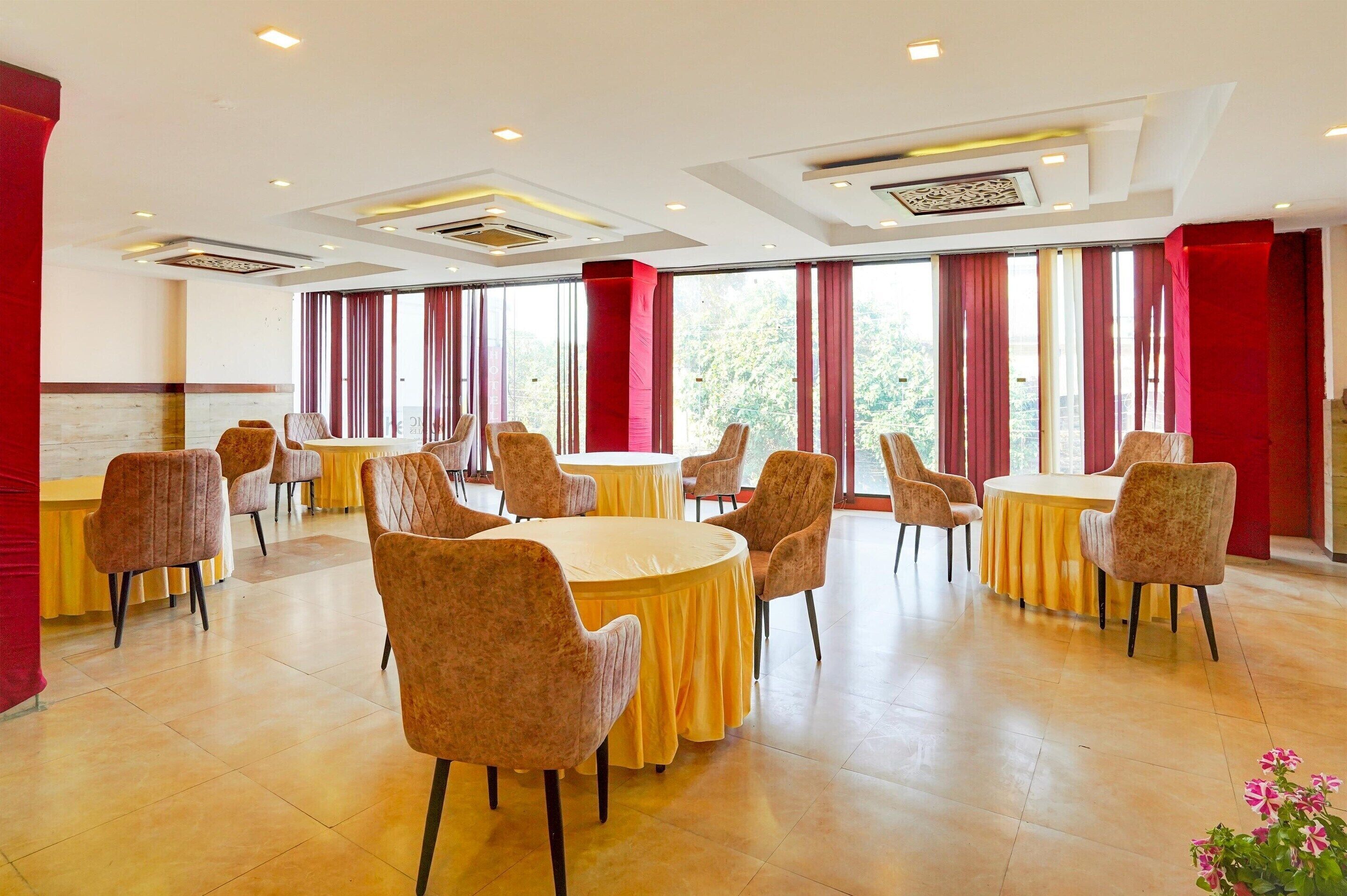 Une salle de conférence d’hôtel avec des tables et des chaises rondes, de grandes fenêtres ornées de rideaux rouges et un design de plafond moderne.