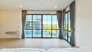 A spacious room with a large sliding glass door leading to a pool area, a bed with white bedding, and a wooden floor. - Chomnok Chomna Pool villa (Khlung)