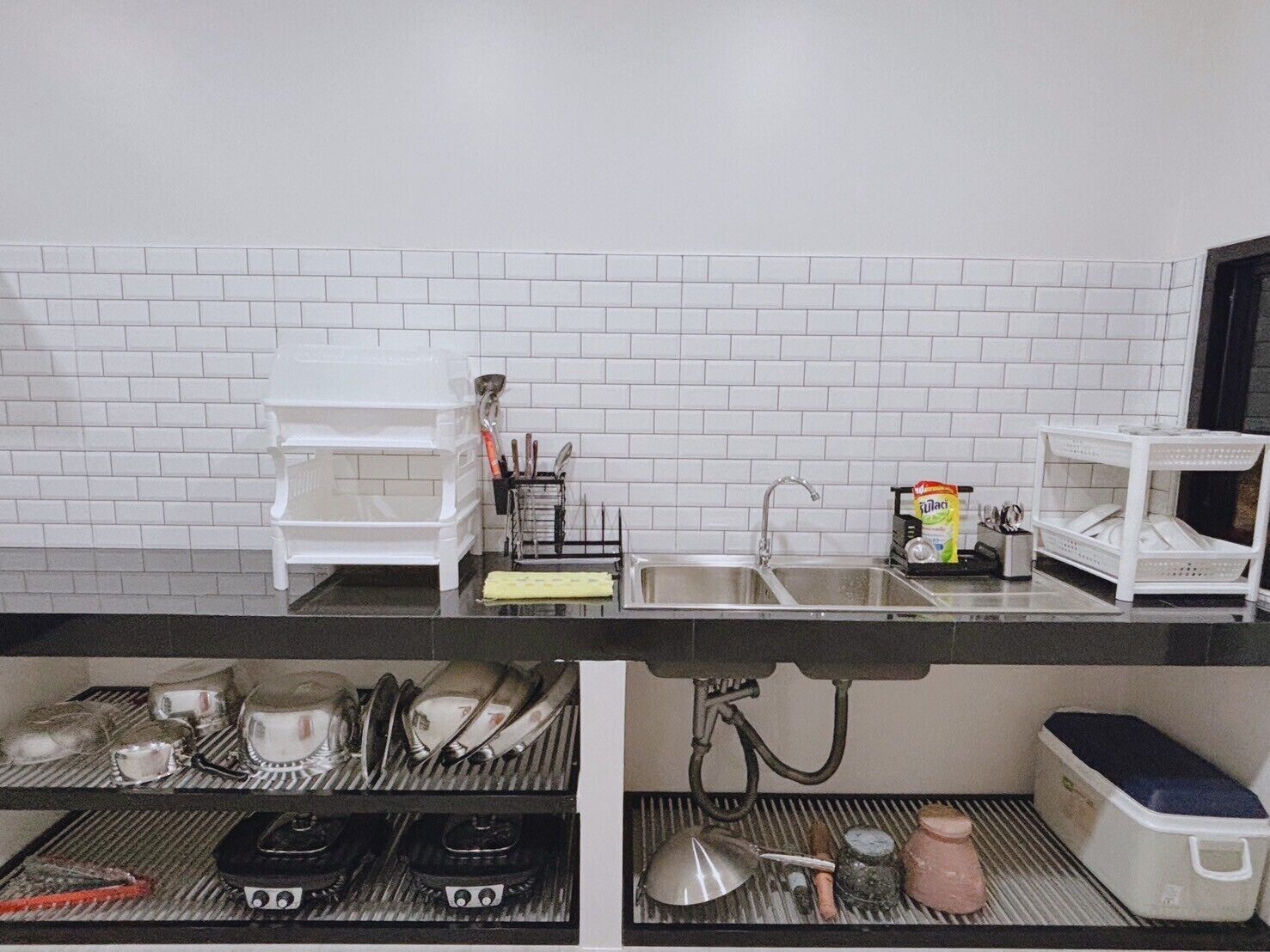 A kitchen with white tiled backsplash, a sink, and a stove. There are utensils and a dish rack on the counter.