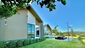 A modern two-story house with large windows, a well-maintained lawn, and a clear view of the surrounding landscape. - Chomnok Chomna Pool villa (Khlung)