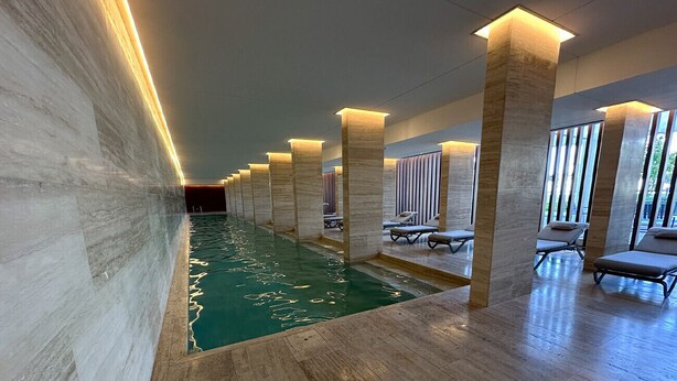 Une piscine avec un mur en marbre d’un côté et une rangée de chaises longues de l’autre.