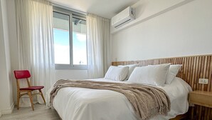 Une chambre à coucher comprenant un lit, une chaise, une fenêtre avec des rideaux et un appareil de climatisation.