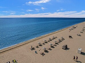 A beach with rows of sun loungers and umbrellas, a clear sky, and the ocean. - Coastal Condo with Resort Service, Pools & Gym 407 (Miami Beach)