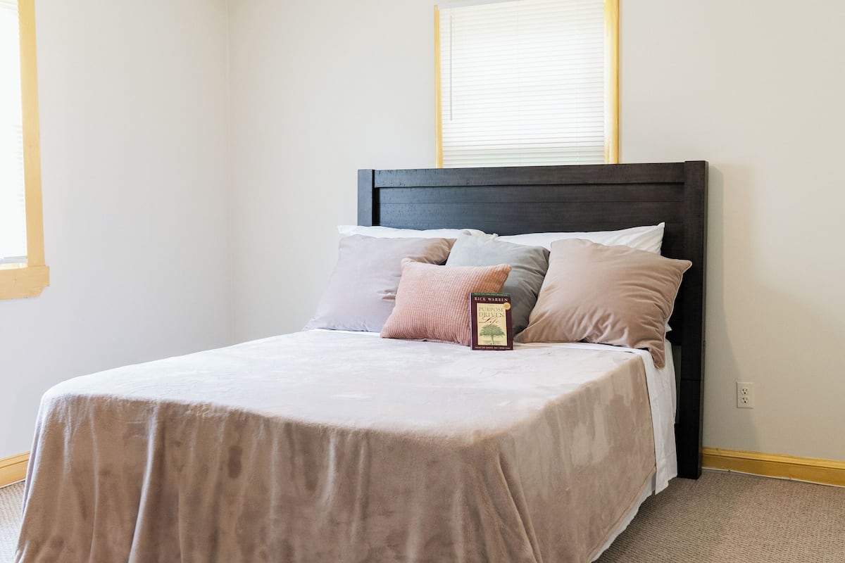 Une chambre à coucher avec un lit, un ventilateur de plafond et une fenêtre avec des stores.