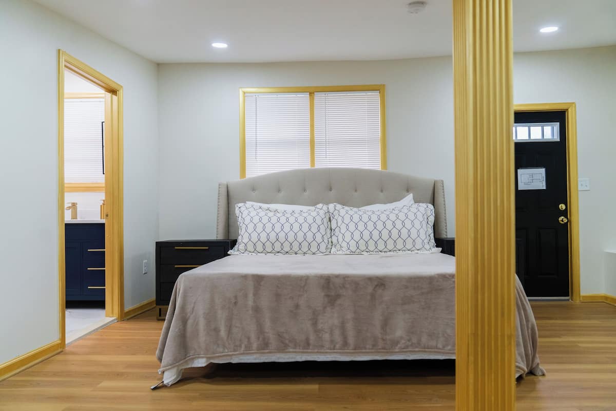Une chambre à coucher comprenant un lit, une table de chevet, une commode et une porte surmontée d’une fenêtre.