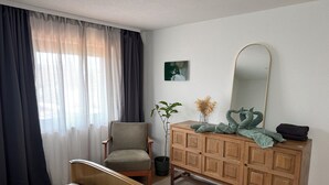 Una camera da letto con un letto, una cassettiera in legno, una sedia, uno specchio e una finestra con tende.