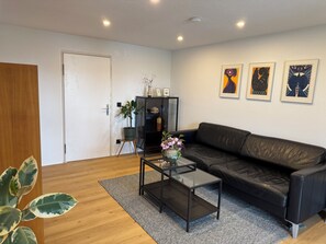 Ett modernt vardagsrum med en svart lädersoffa, ett soffbord i glas och en krukväxt.