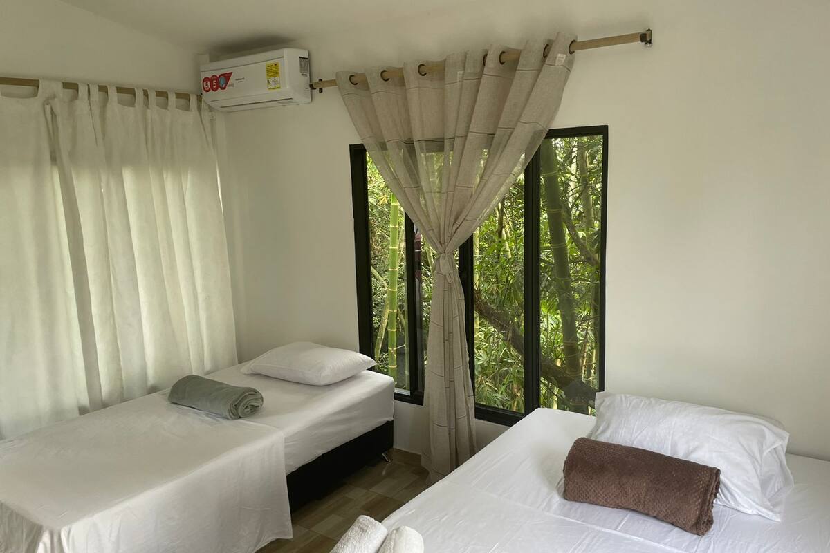 A room with two beds, a window with curtains, and an air conditioning unit.