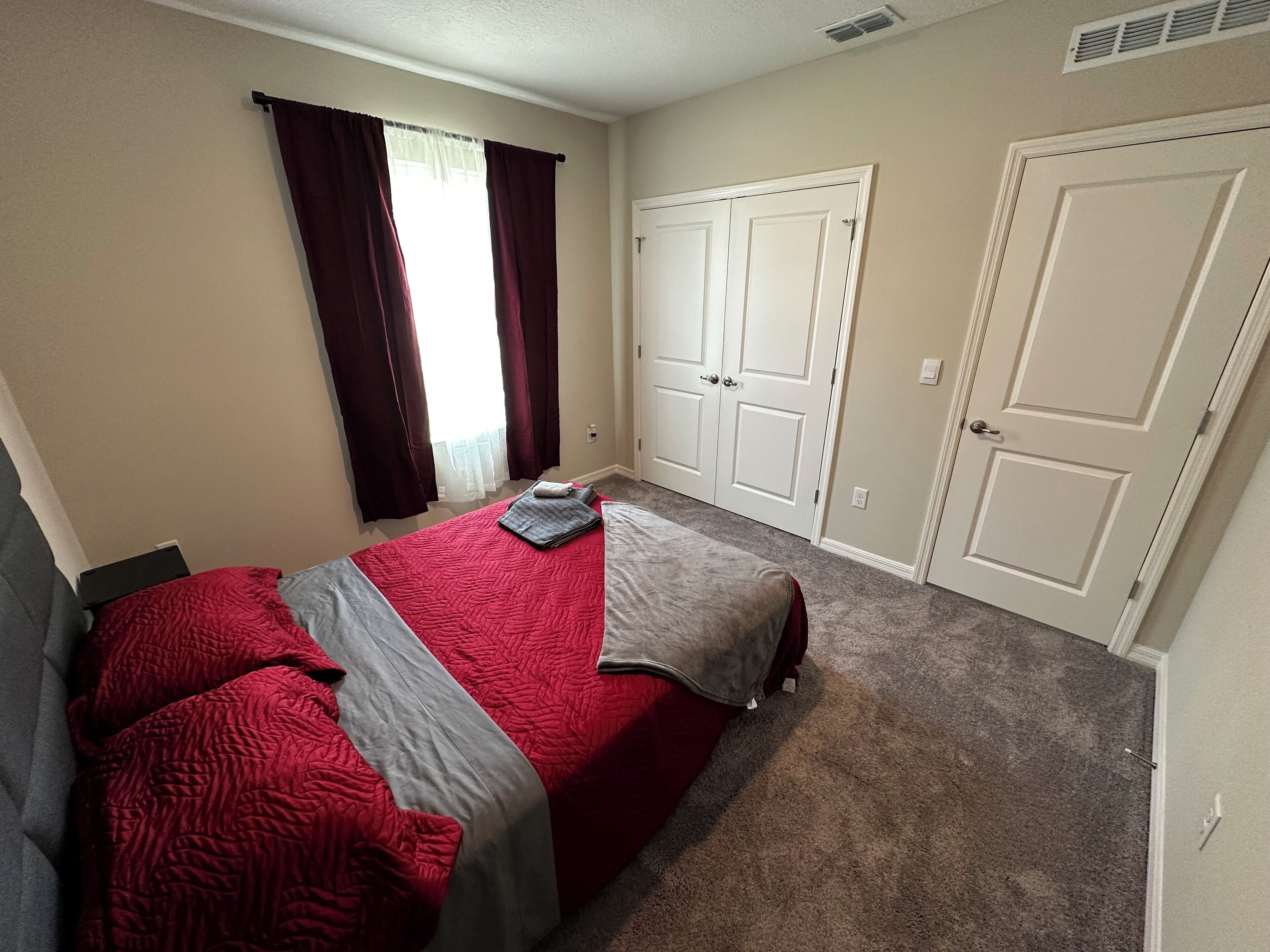 Un dormitorio con una cama, dos puertas y una ventana con cortinas.