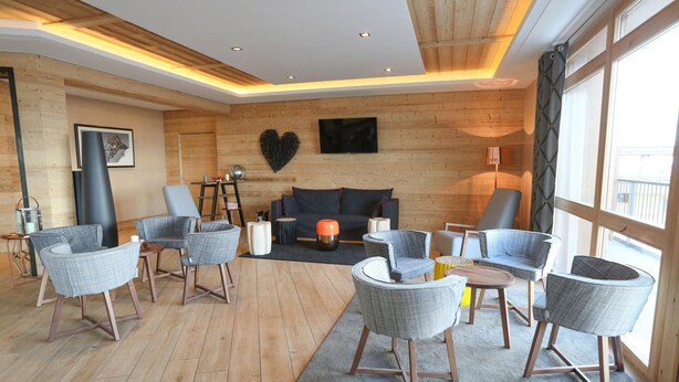 Una sala de estar moderna con paredes de madera, un sofá gris y varios sillones grises.