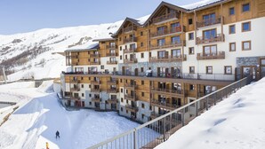 A multi-story hotel with balconies, wooden exterior, and a ski slope in the background. - Apartment in France With Heated Pool & Spa (Les Belleville)