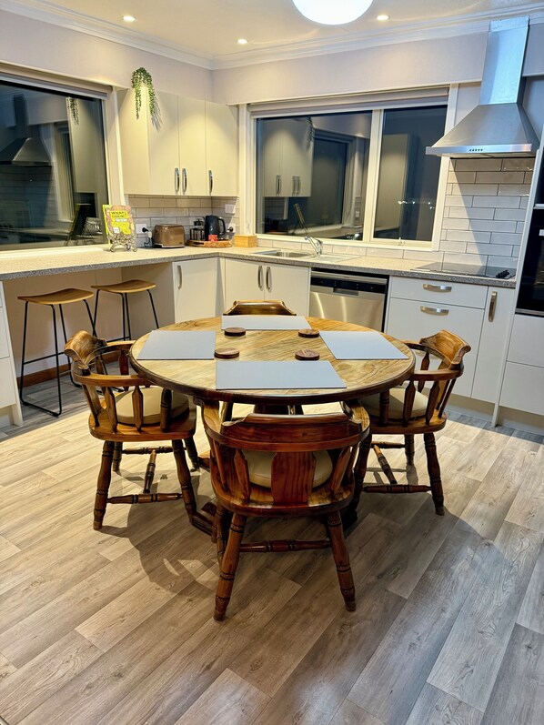 A modern kitchen with a round dining table, wooden chairs, and a built-in dishwasher.