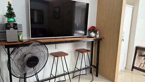 A modern kitchen with a large flat-screen TV mounted on a wooden countertop, a small Christmas tree, and a fan.