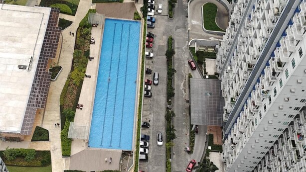 A high-rise residential building with multiple balconies, a swimming pool, and a parking area.