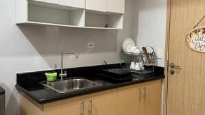 A kitchen with white cabinets, a black countertop, a stainless steel sink, and a wooden door with a sign.