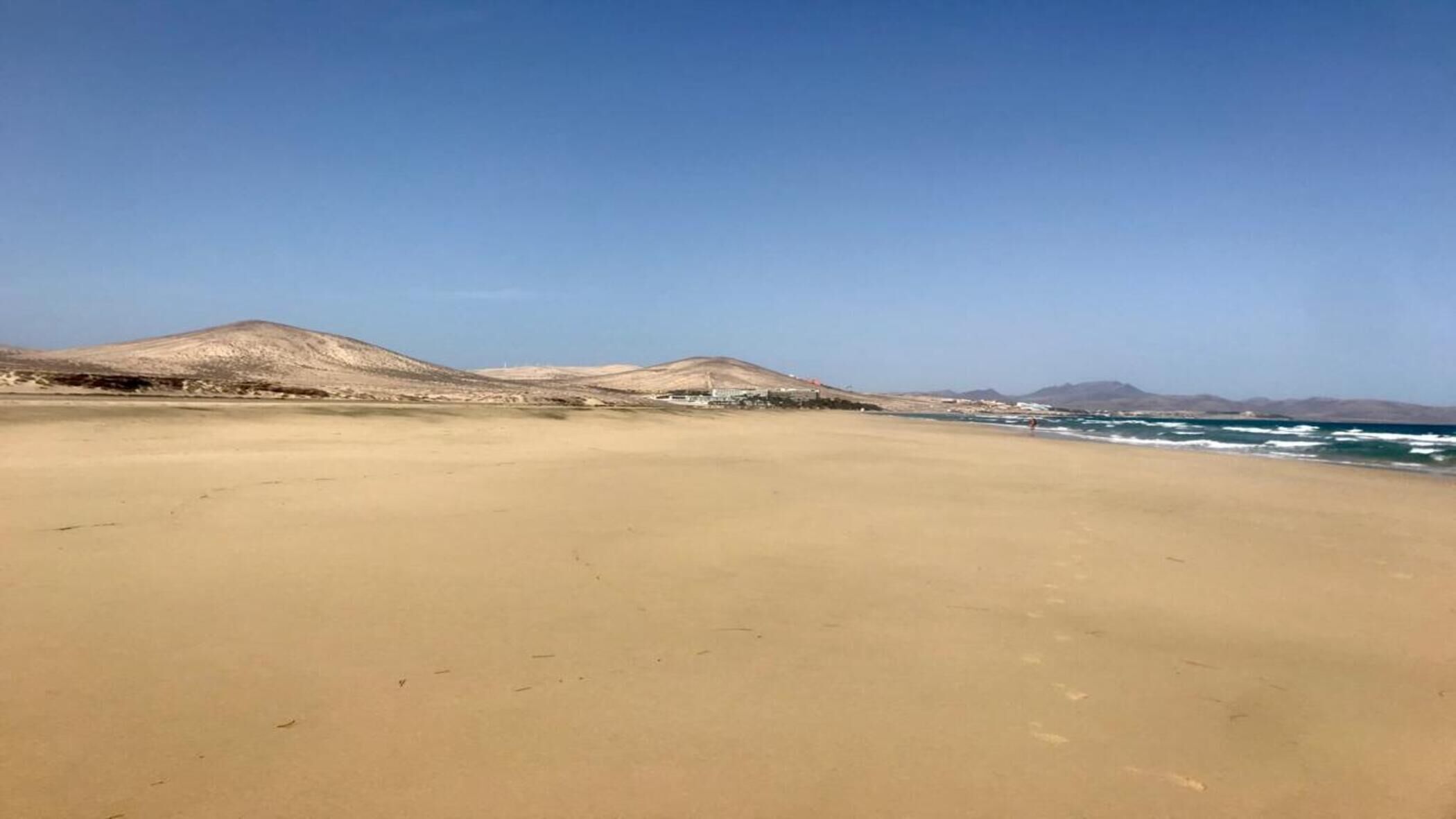 A wide sandy beach with distant hills and a clear sky.