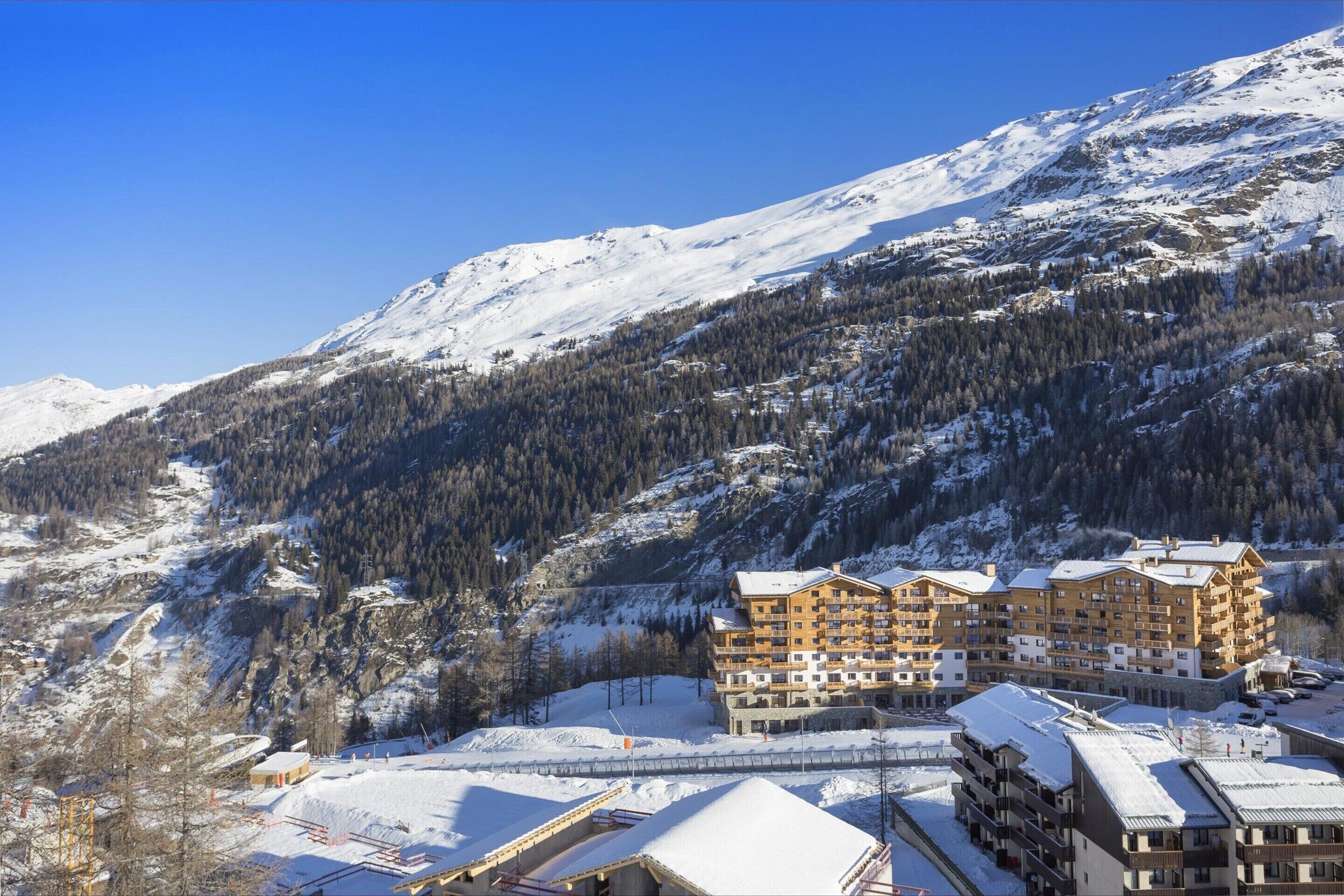 Een hotel met meerdere verdiepingen, met op de achtergrond een met sneeuw bedekte berg, met een centrale binnenplaats en een skipiste.