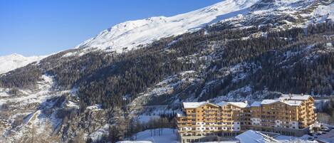 Een hotel met meerdere verdiepingen, met op de achtergrond een met sneeuw bedekte berg, met een centrale binnenplaats en een skipiste.