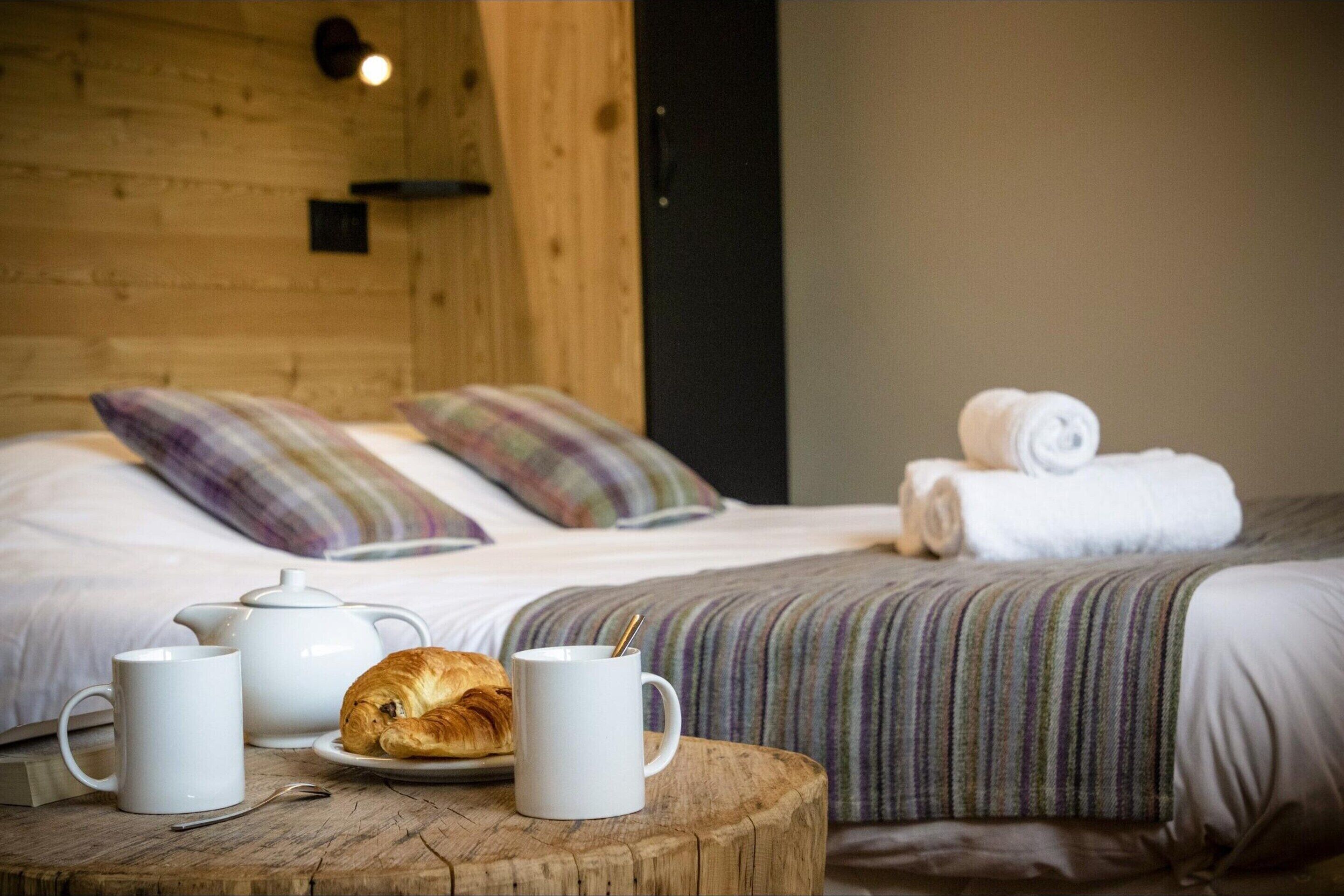 A neatly made bed with a striped blanket, a rolled-up towel, and a croissant on a wooden table.