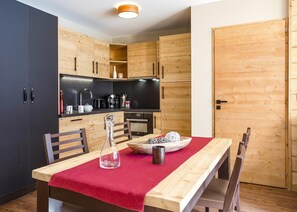 A compact kitchen with wooden cabinets, a black countertop, and a dining table with a red tablecloth.