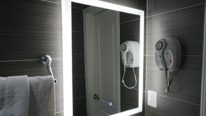 A bathroom with a large mirror, a towel rack, and a hairdryer mounted on the wall. - Avenue Motel (Gardena)