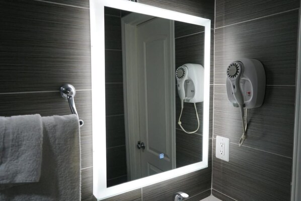 Une salle de bain avec un grand miroir, un porte-serviettes et un sèche-cheveux fixé au mur.