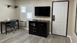 A compact room with a desk, chair, TV, and a door. - Avenue Motel (Gardena)