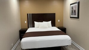 A hotel room with a large bed, a dark headboard, and a framed picture on the wall. - Avenue Motel (Gardena)