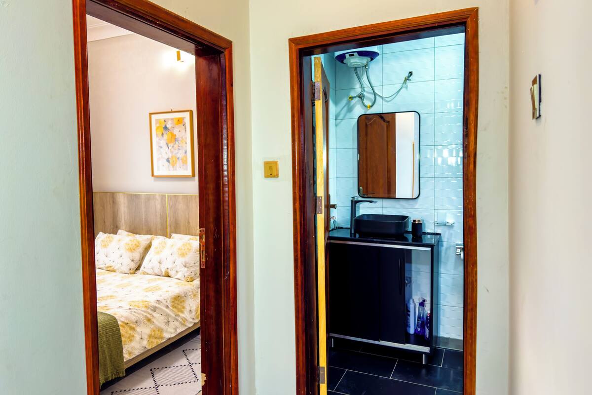 A bedroom with a bed and a bathroom with a sink and mirror.